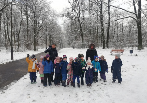 Na zdjęciu widać dzieci oraz panie z grupy na spacerze w parku. W tle drzewa i śnieg.